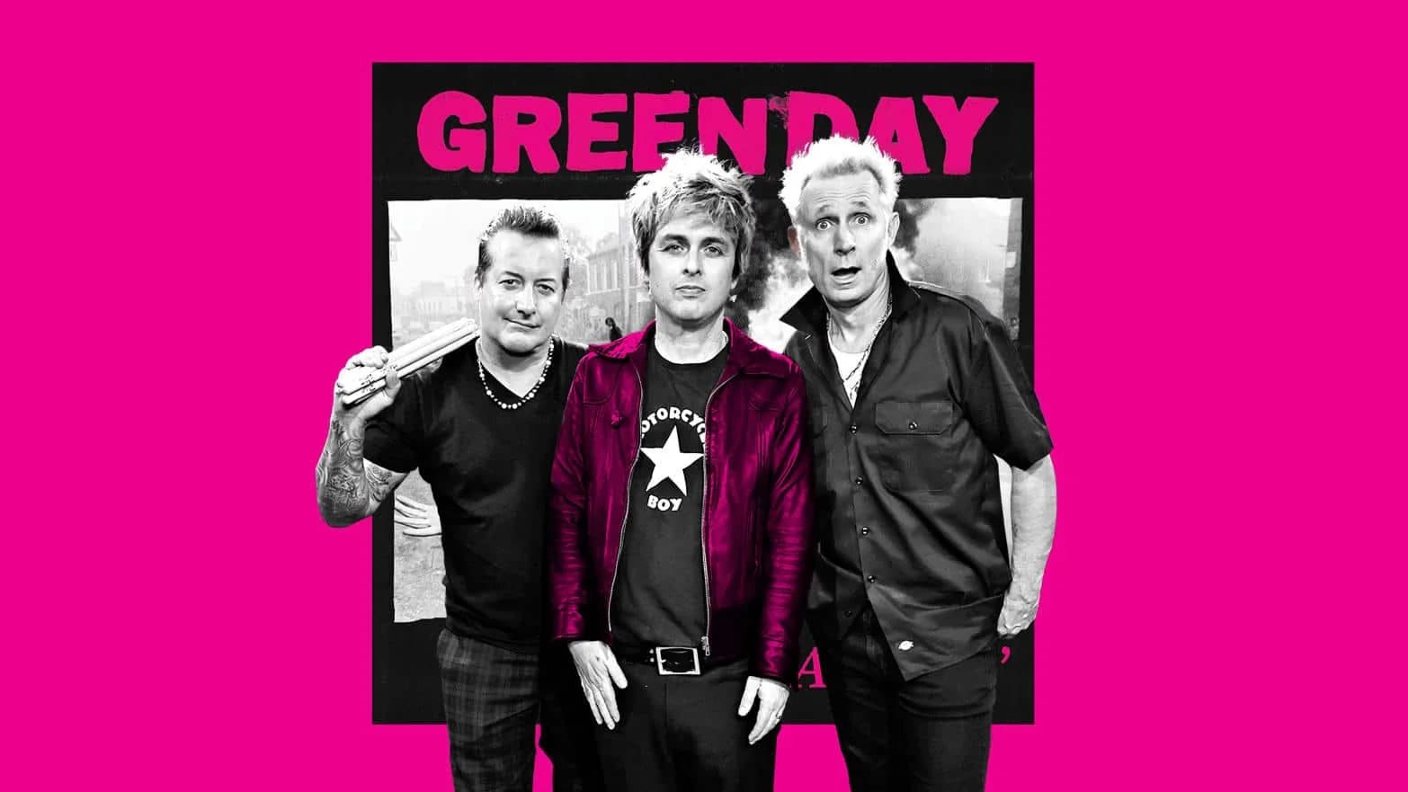 Three band members stand together in front of a pink background with the words "GREEN DAY" in bold letters. One person holds drumsticks, another wears a star-themed shirt and a red jacket, and the third sports a dark button-up shirt.