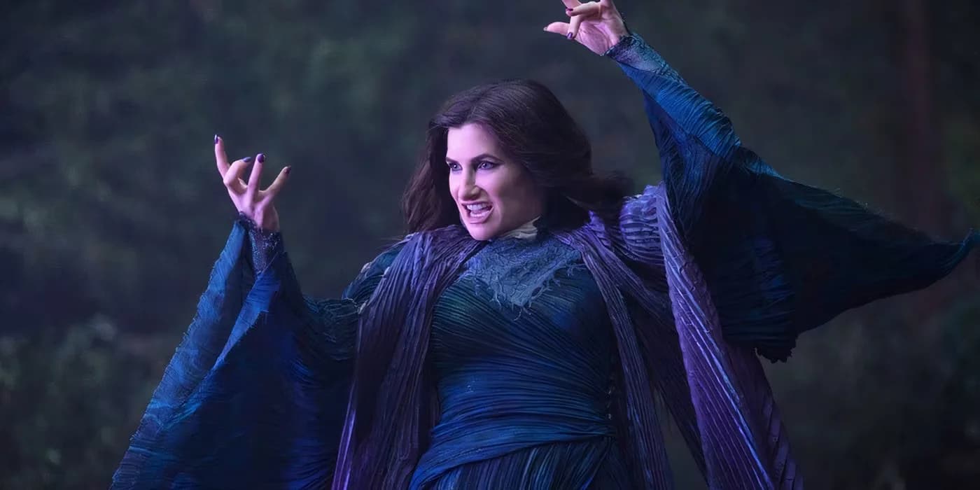 A woman with long dark hair, wearing a flowing purple and blue robe, raises her hands dramatically against a blurred background of trees.