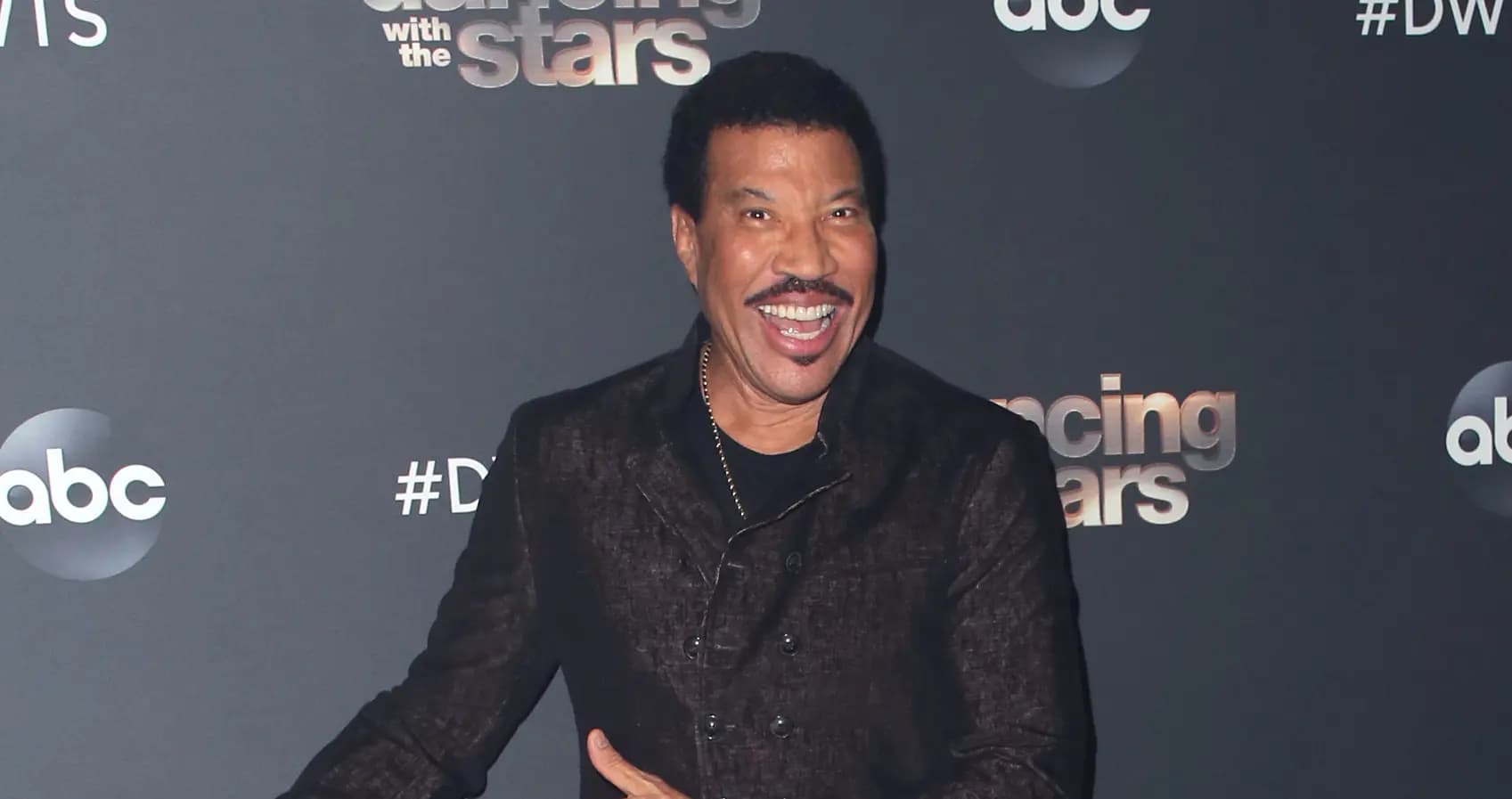 A person smiling widely at a 'Dancing with the Stars' event, standing in front of a backdrop featuring the show's logo and ABC logo.