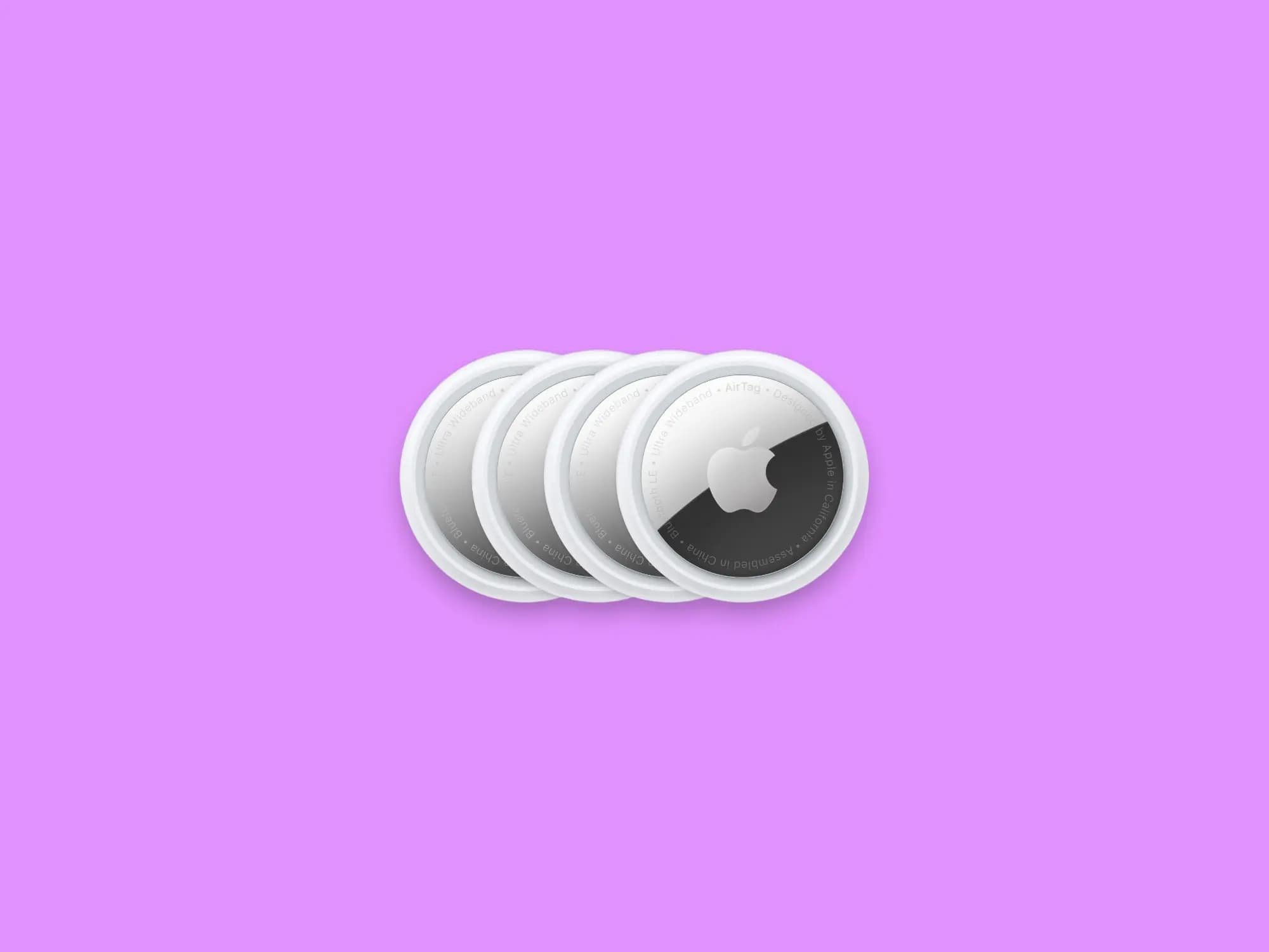 Four white Apple AirTags arranged in a row on a purple background.