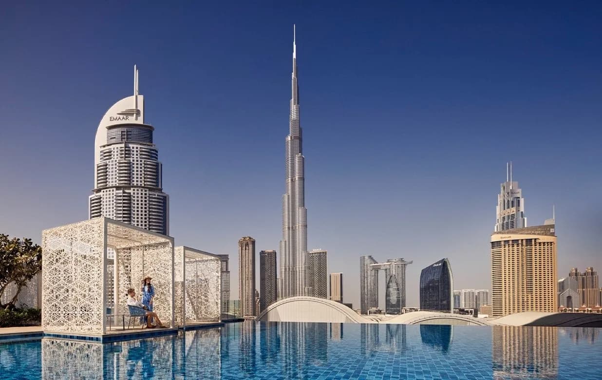 A rooftop pool with a woman sitting in a stylish cabana, overlooking a city skyline dominated by the Burj Khalifa.
