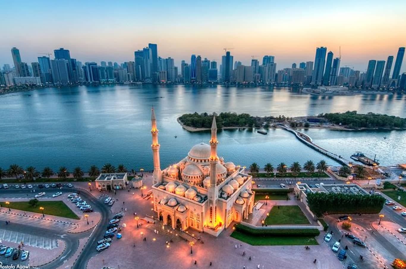 Lit mosque by the waterfront with a city skyline across the bay at sunset
