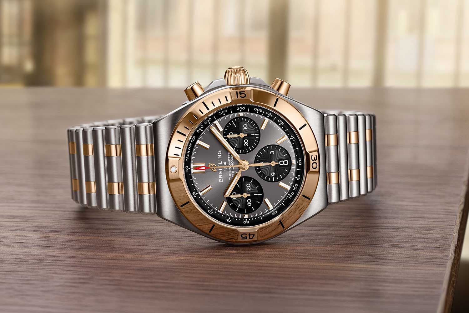 Luxury stainless steel and gold chronograph wristwatch on a wooden table, displayed front-facing