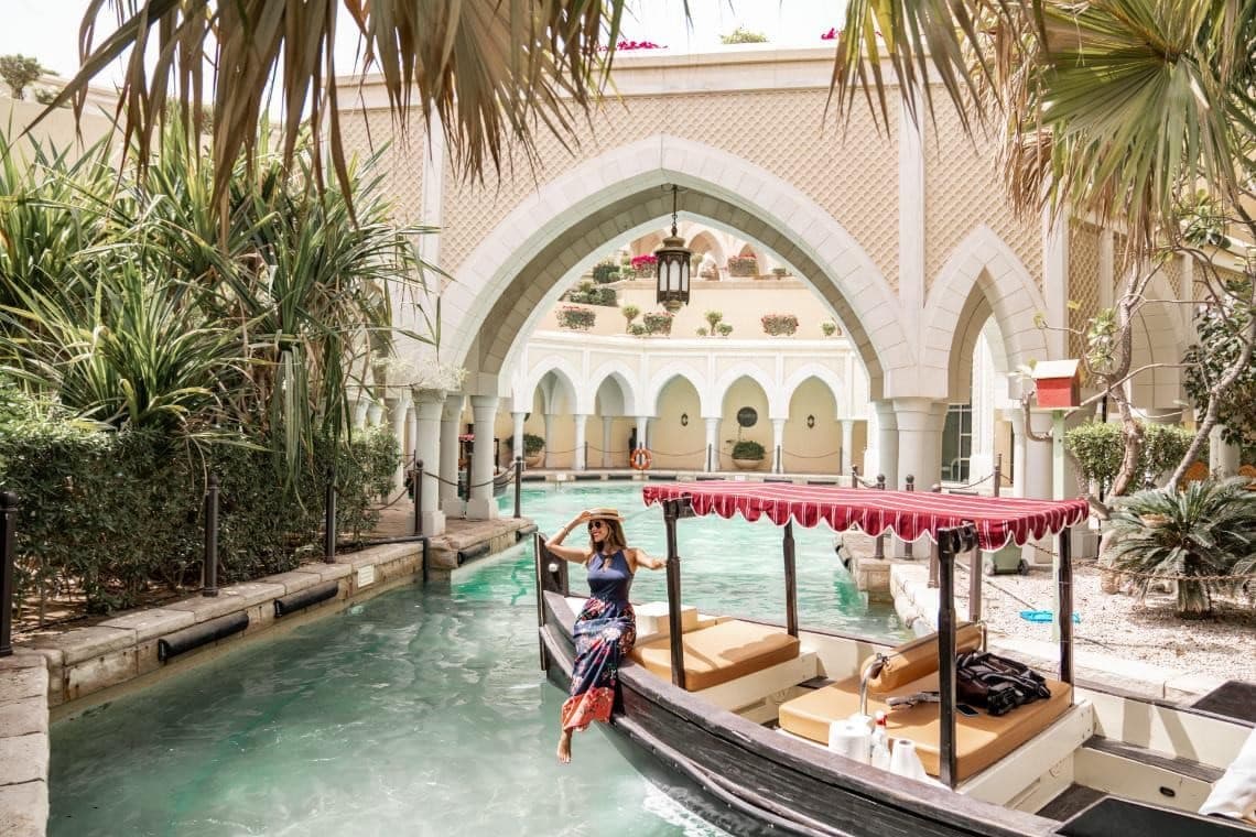 Woman relaxing on a gondola in a hotel courtyard canal with arches and tropical plants