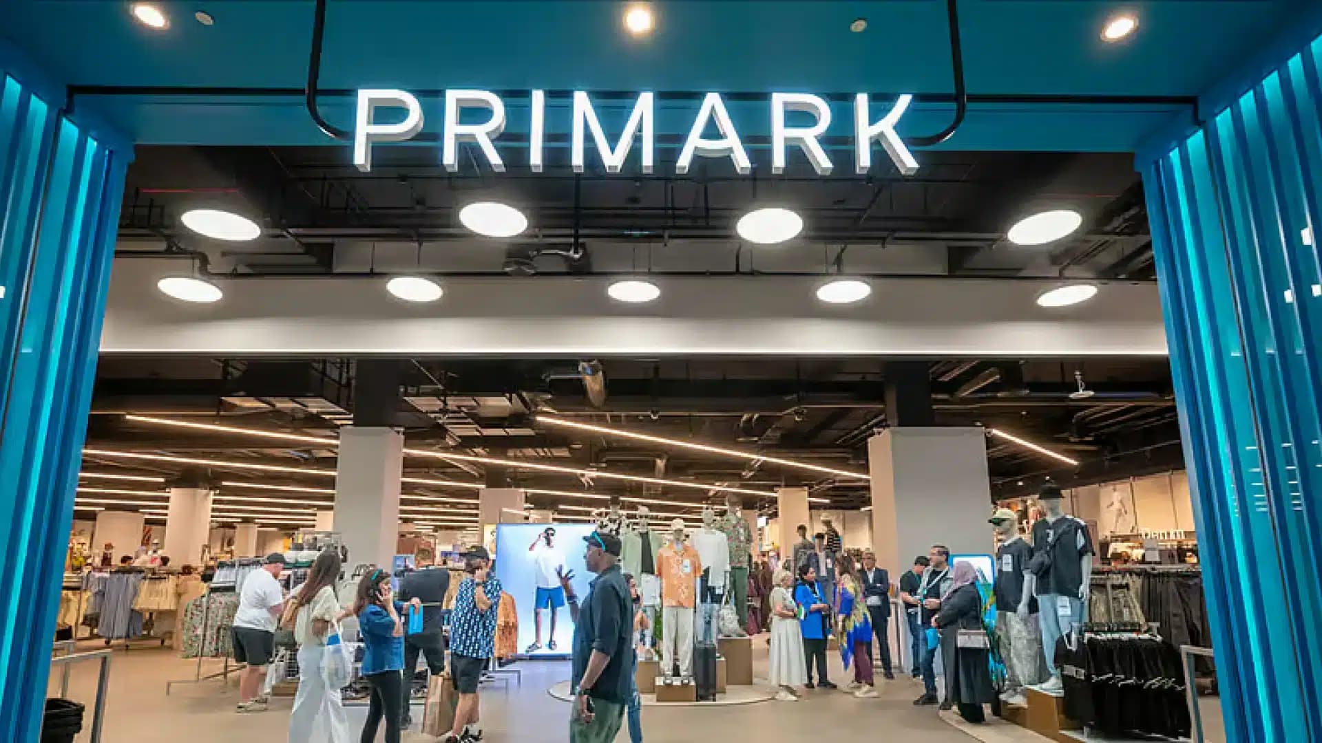Busy Primark store entrance with shoppers, mannequins, and bright blue framing lights
