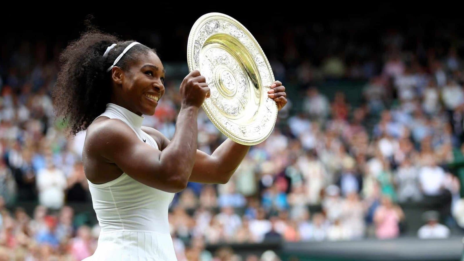 Tennis player Serena Williams smiling and holding up the Wimbledon championship trophy after a win