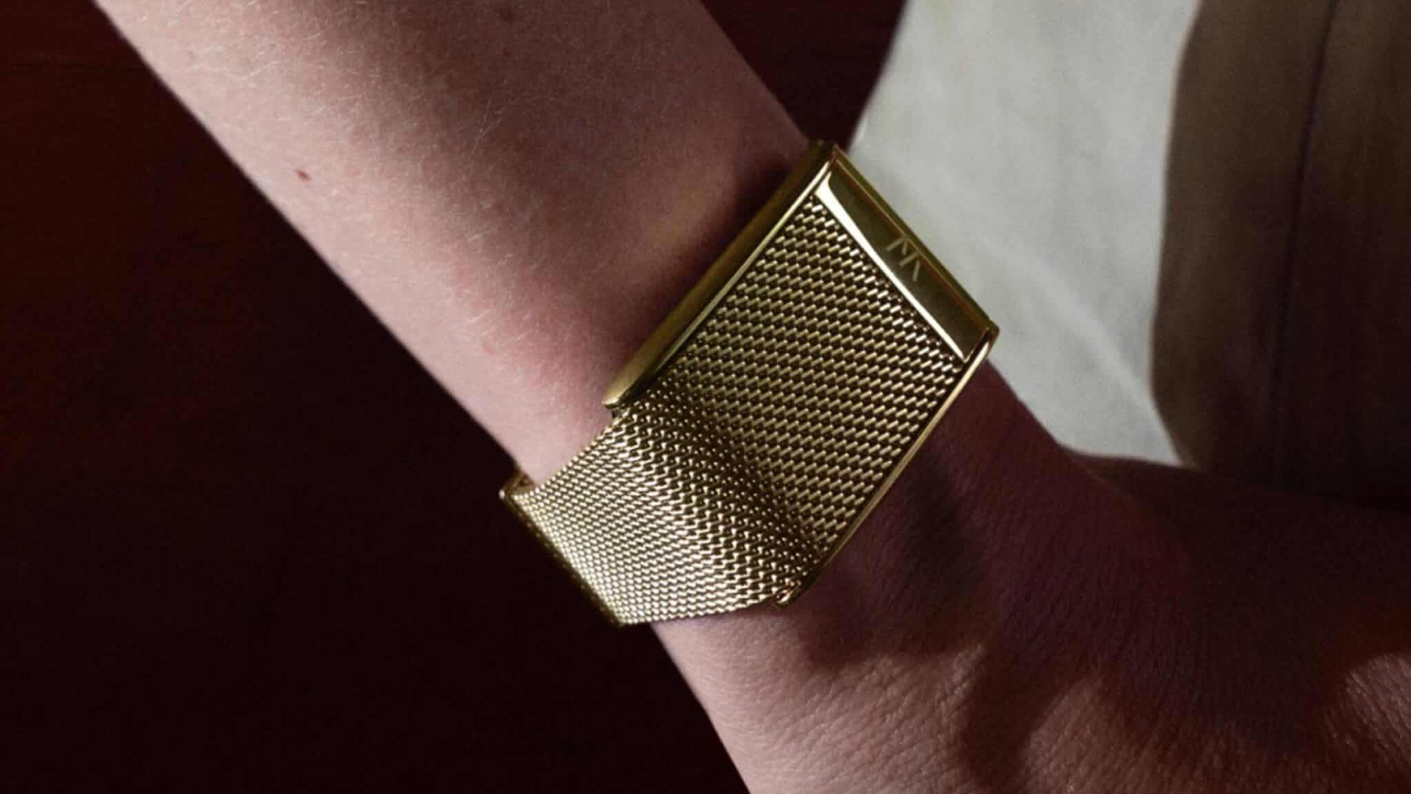 Gold-toned metal bracelet watch with a textured rectangular face on a person’s wrist