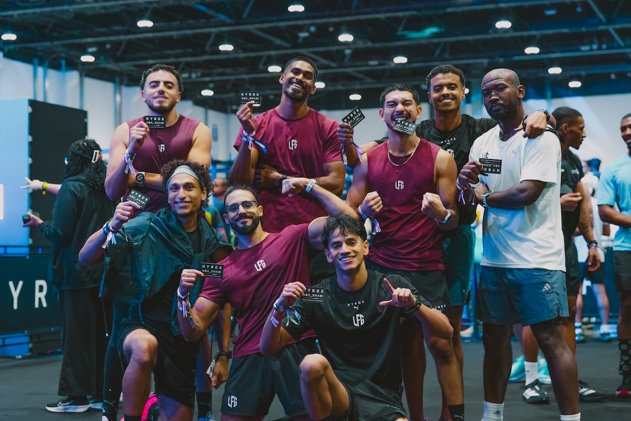 Group of athletes posing with HYROX Abu Dhabi cards at an indoor fitness event