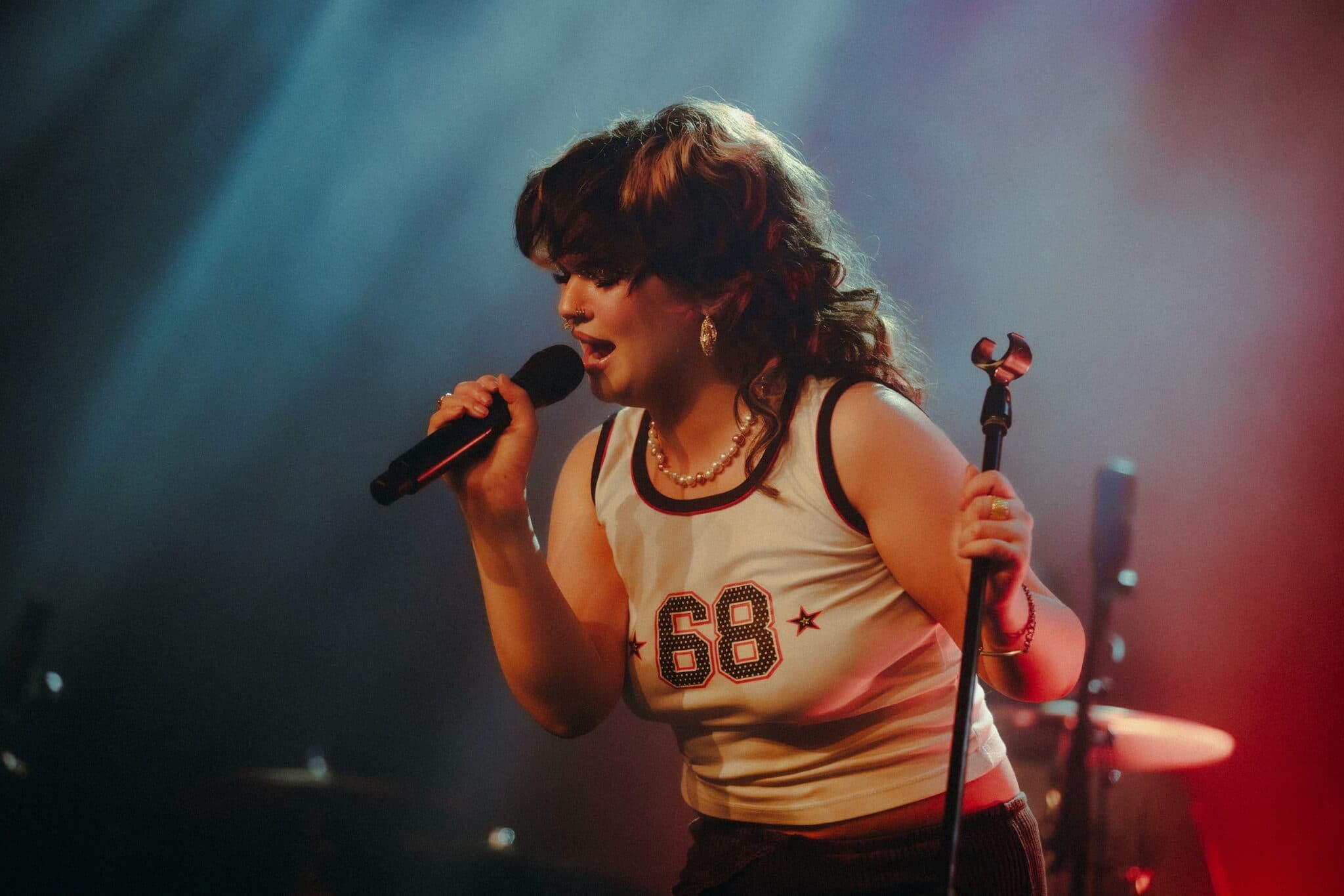Singer performing into a microphone onstage under blue and red lighting