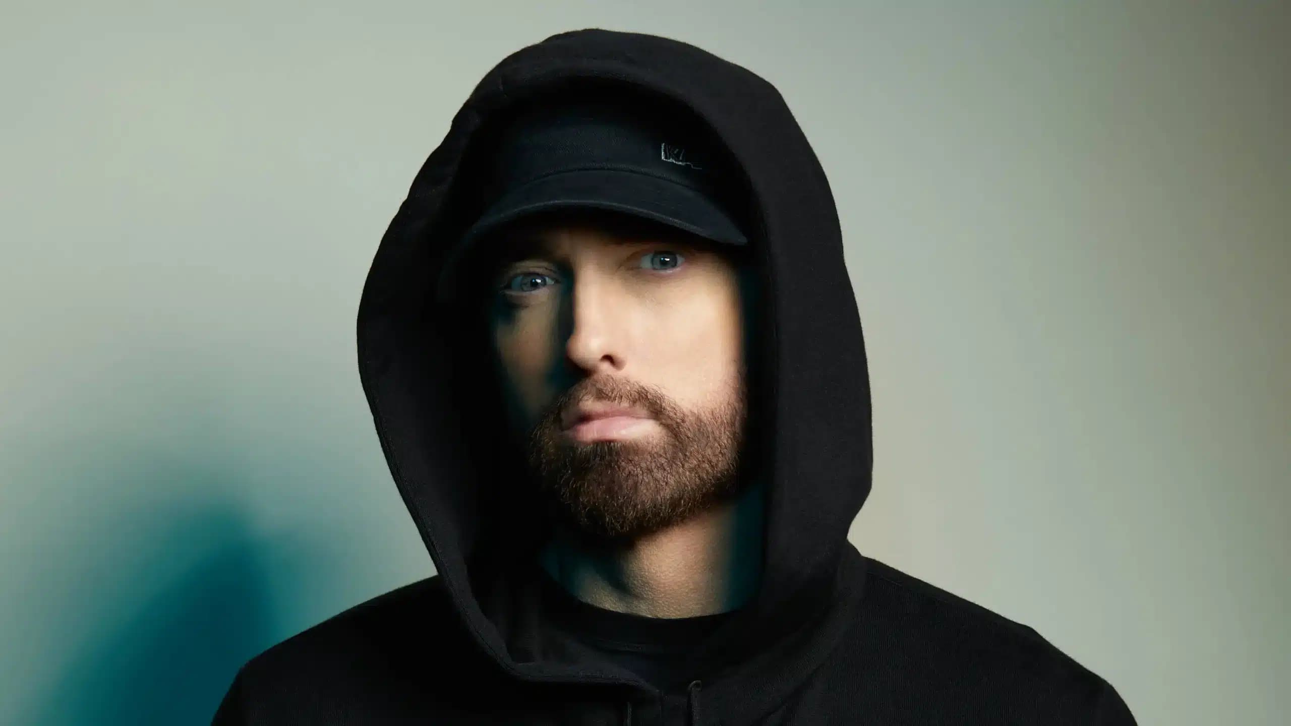 A person wearing a black hoodie and a black cap, with a neutral expression, looking towards the camera.
