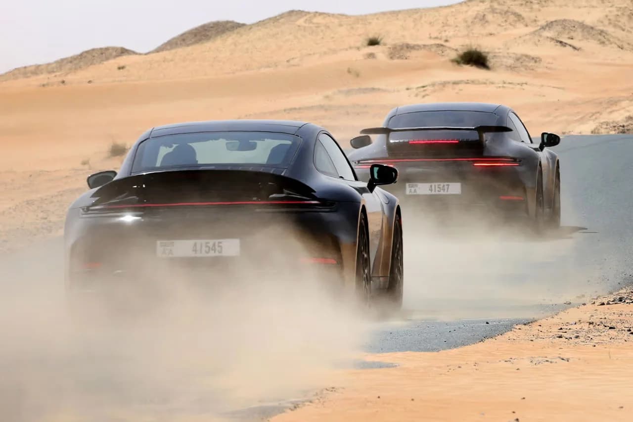 Two sports cars driving on a dusty desert road, kicking up clouds of dust behind them.