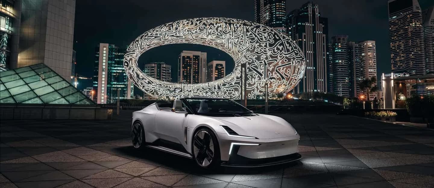A sleek white sports car parked in front of a futuristic oval building with illuminated Arabic calligraphy at night, surrounded by towering skyscrapers.