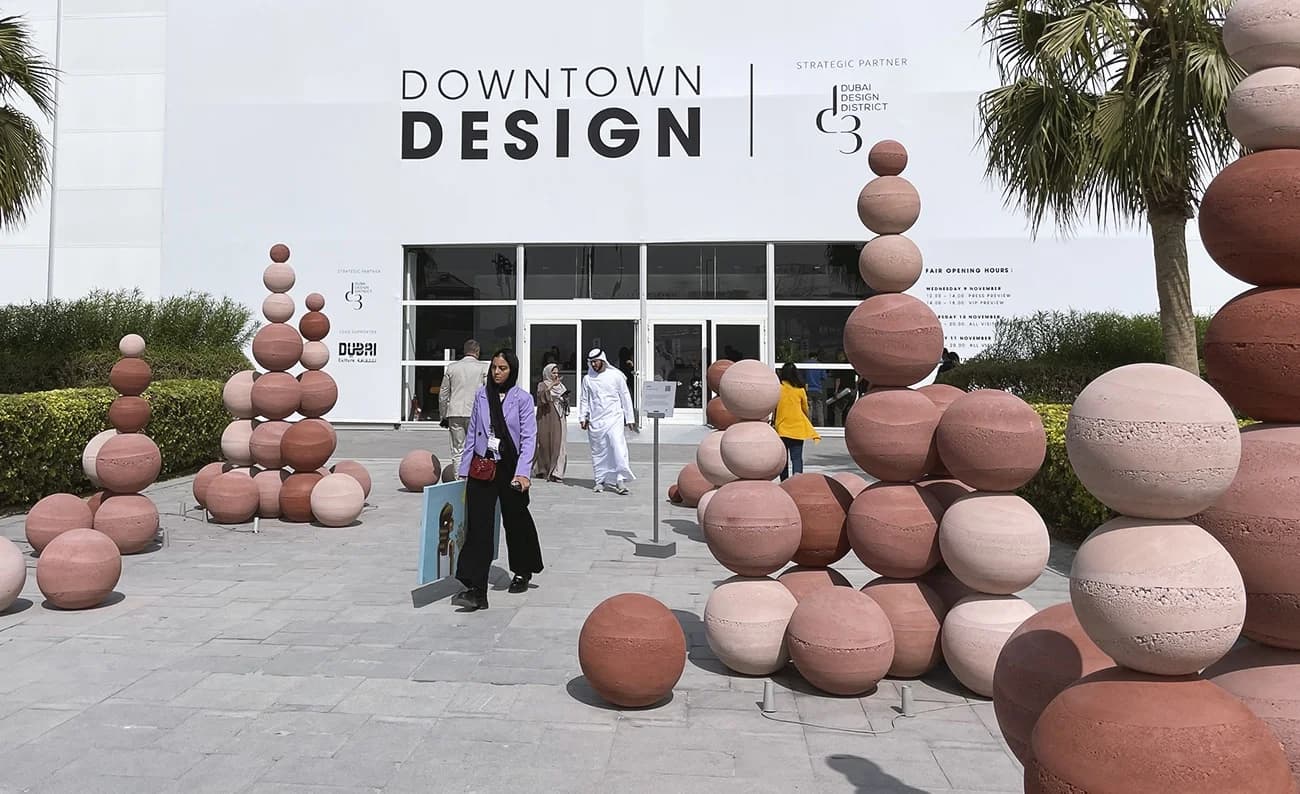 Visitors walking outside a building marked 'Downtown Design' with stacks of red and pink spherical sculptures arranged in clusters around the area.