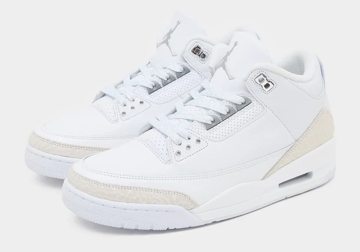 A pair of white sneakers featuring a sleek design with textured detailing, a perforated leather upper, and a visible air cushioning system in the sole.