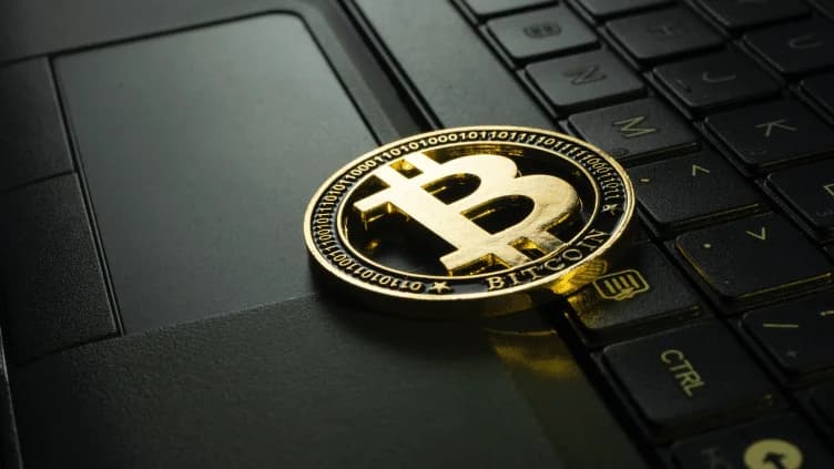 A gold Bitcoin coin resting on a black laptop keyboard, highlighting the cryptocurrency theme in a tech environment.