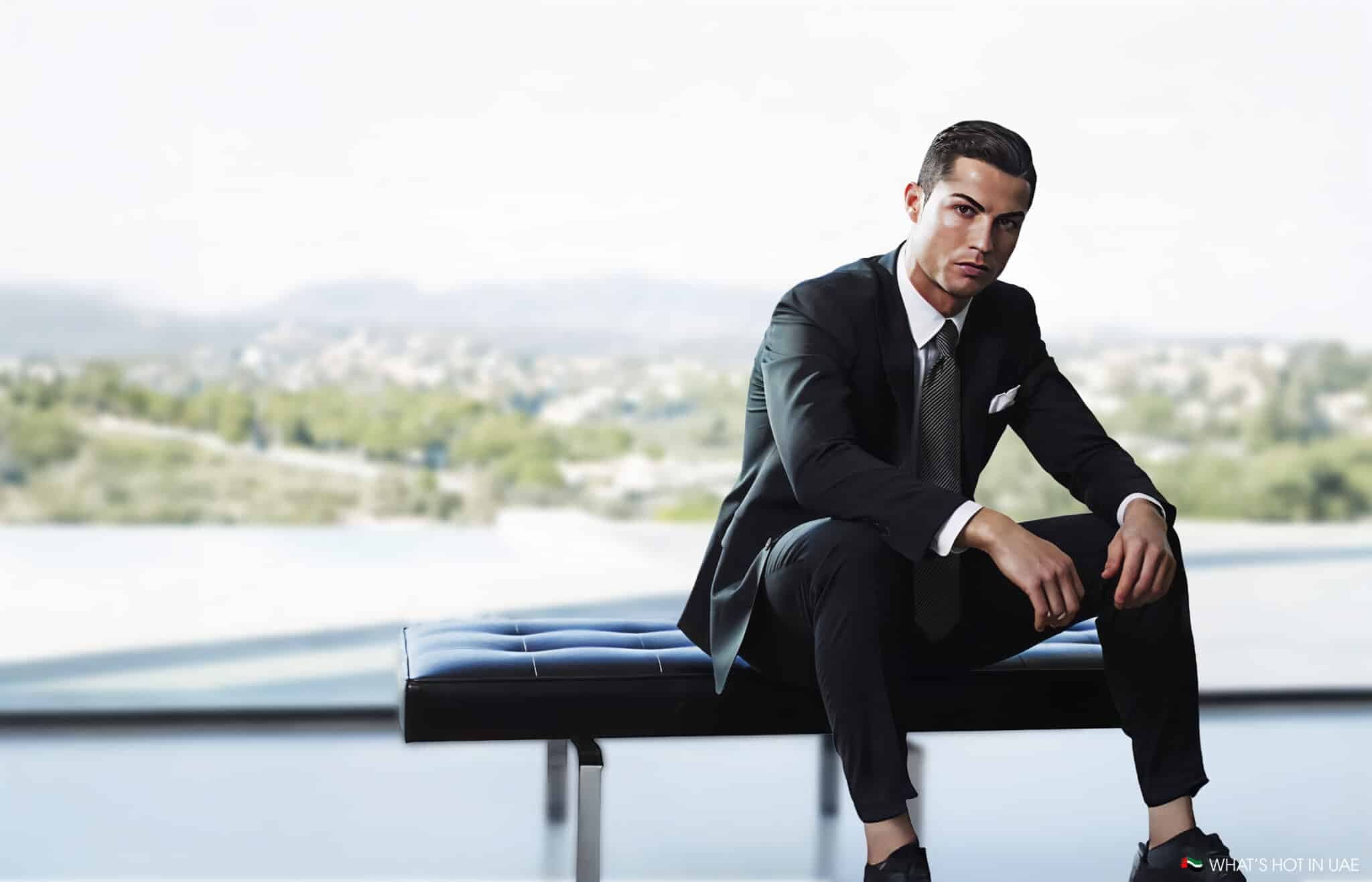 A man in a suit sits on a modern bench in front of a large window with a blurred outdoor view.