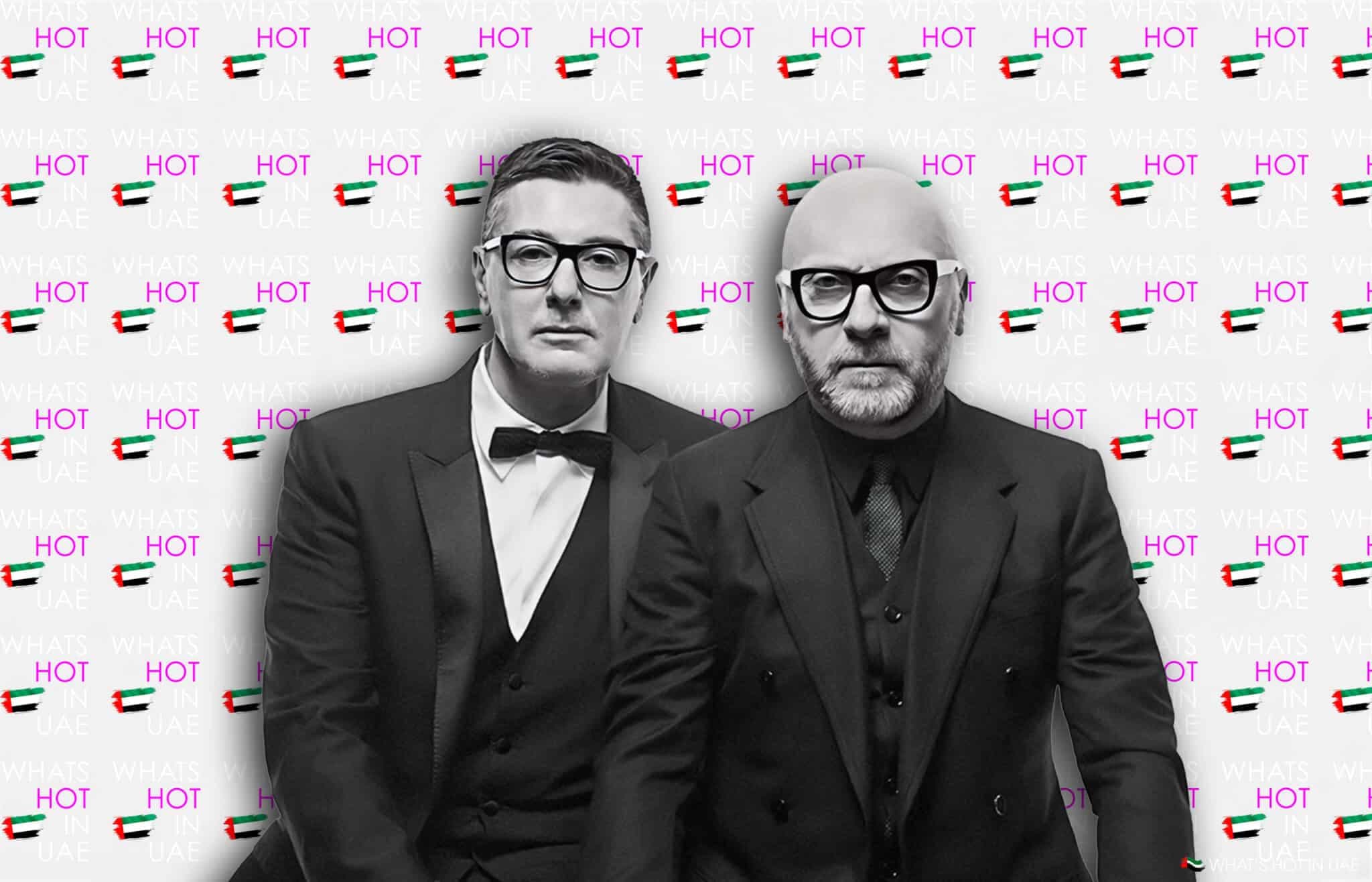 Two men in black suits and glasses stand in front of a backdrop with repeated text "WHAT'S HOT IN UAE" and images of the UAE flag.