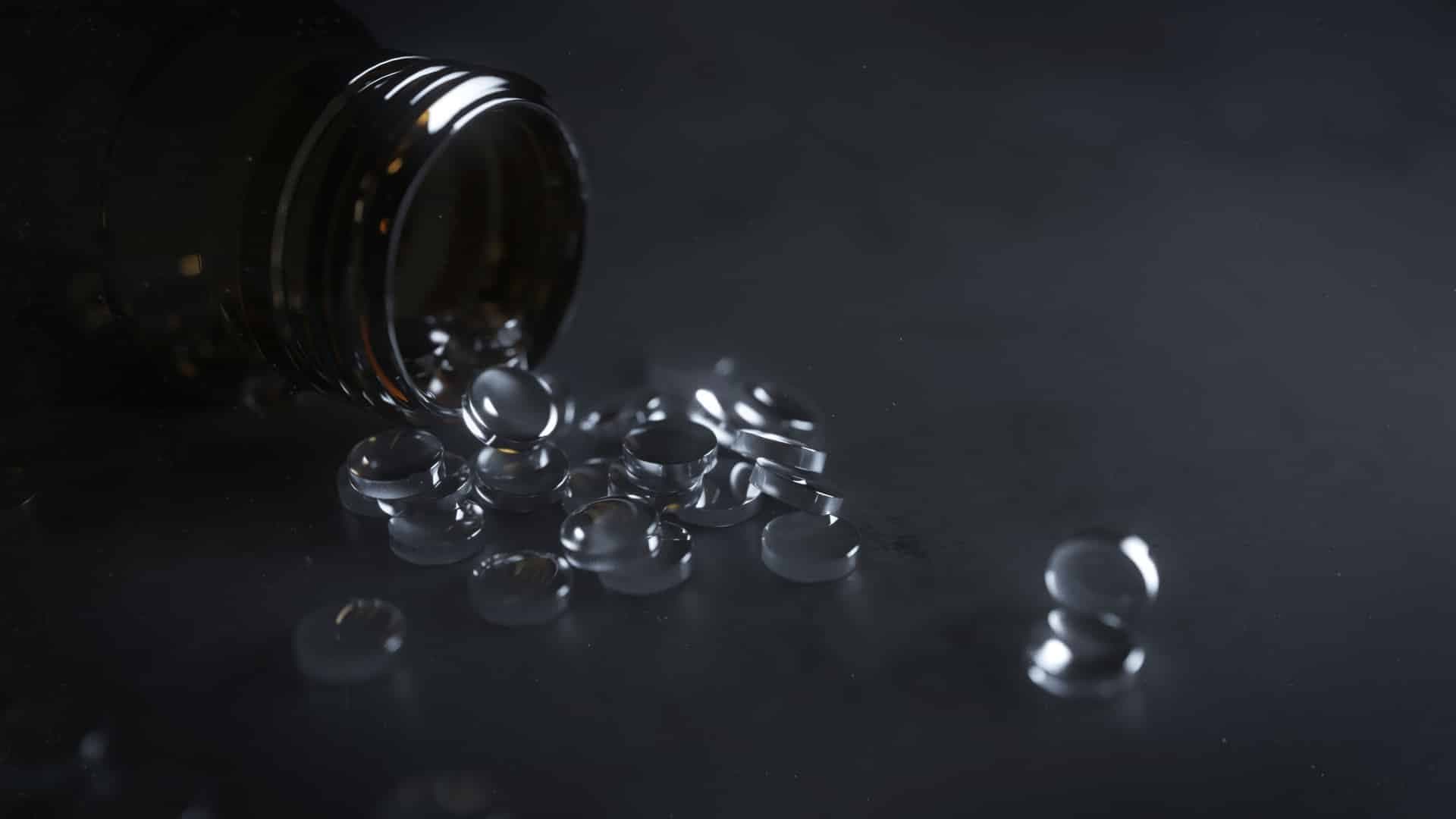 A dark glass bottle tipped over with clear gel capsules spilling out onto a dark surface.