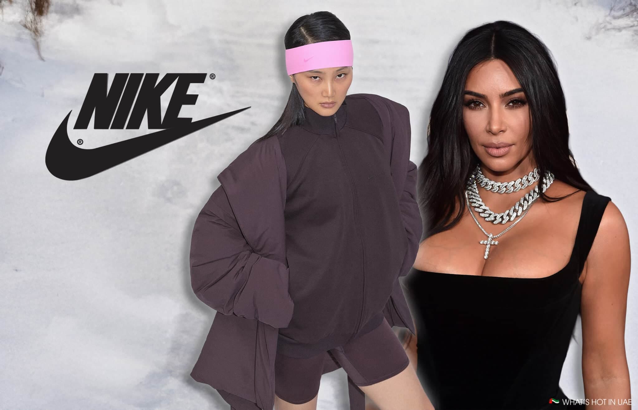 A fashion model wearing a Nike outfit with a pink headband stands next to a woman in a black dress with layered necklaces in front of a snowy background with the Nike logo displayed prominently.