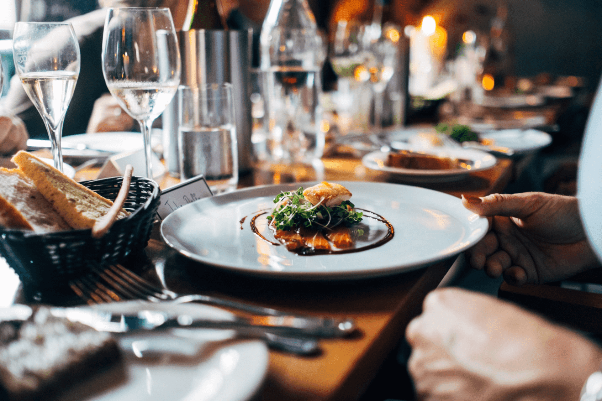 A gourmet dish with greens and sauce is served on a plate at a sophisticated dining setting with glasses and bread.