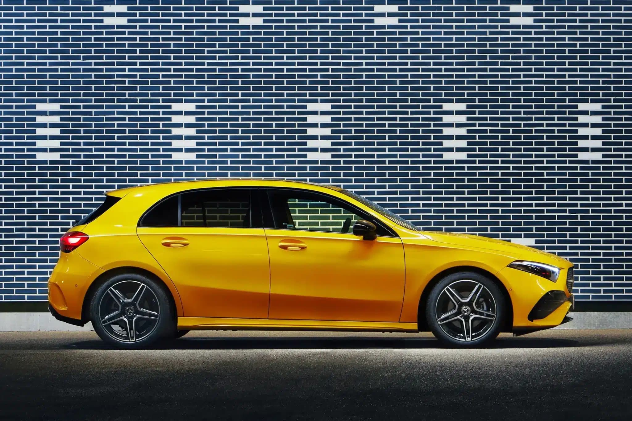 A bright yellow hatchback car parked in front of a patterned brick wall.