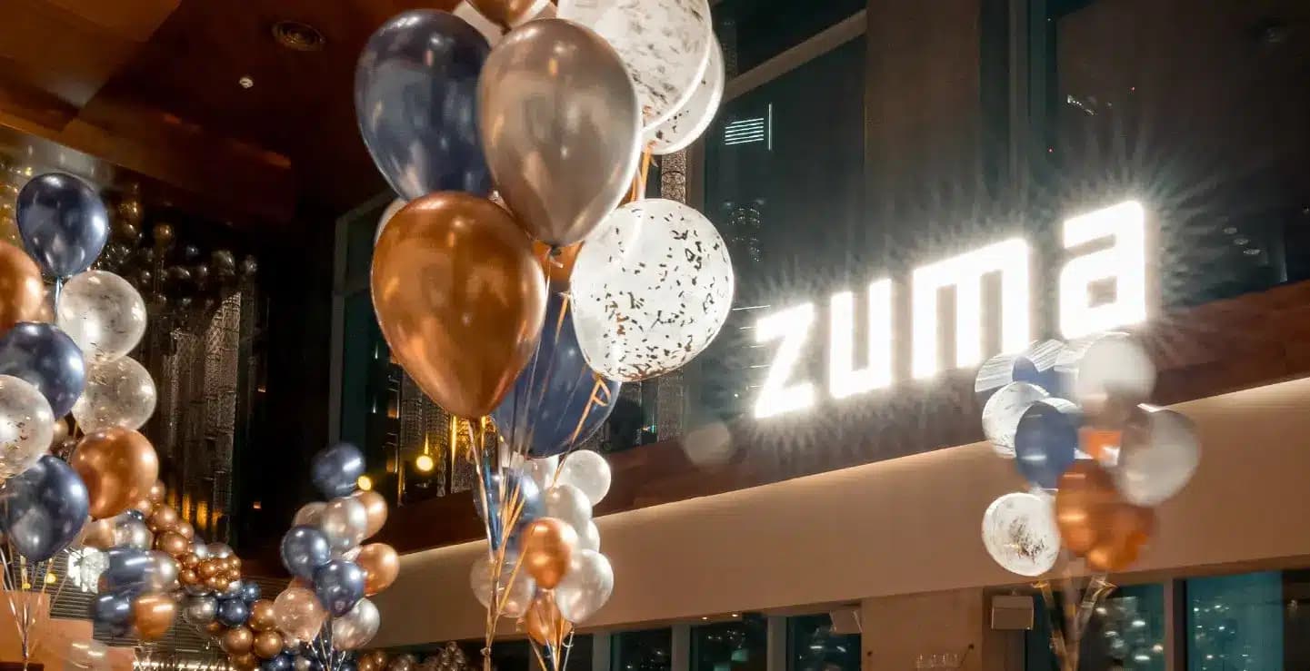 Balloons in blue, gold, and white decorate an indoor space with a bright "zuma" sign on a wall.