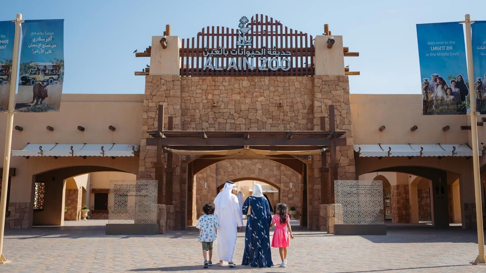 Family walking toward the entrance of Al Ain Zoo under a clear blue sky