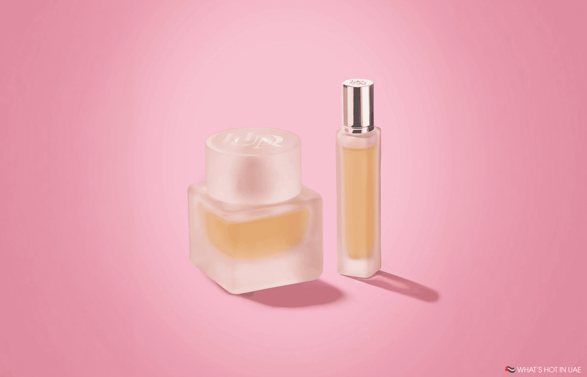 Two frosted perfume bottles with gold liquid on a pink background