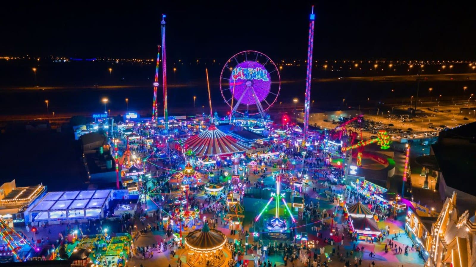 A vibrant night view of a colorful amusement park with a large Ferris wheel and various lit-up rides.