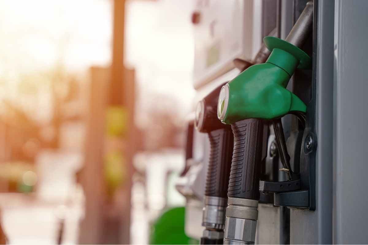 Green fuel pump nozzle at a gas station with a blurred background.