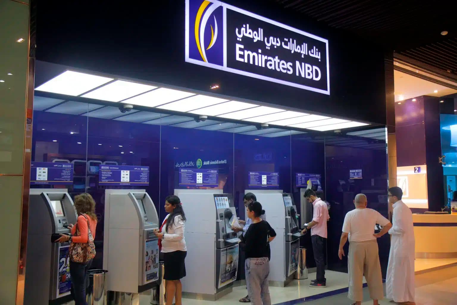People using ATMs at an Emirates NBD branch, with a blue and white sign overhead.