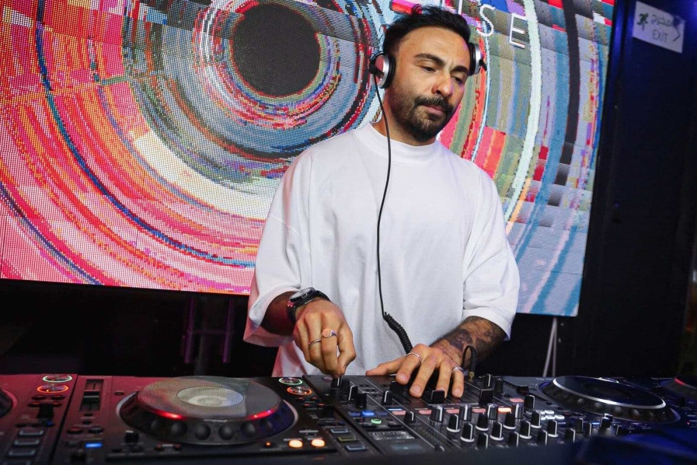 DJ wearing headphones mixing music on a controller in front of a colorful abstract screen
