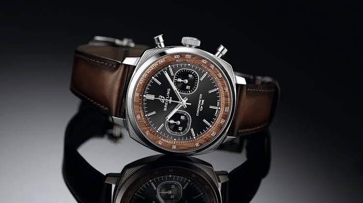 Luxury Breitling chronograph wristwatch with brown leather strap on a reflective black surface