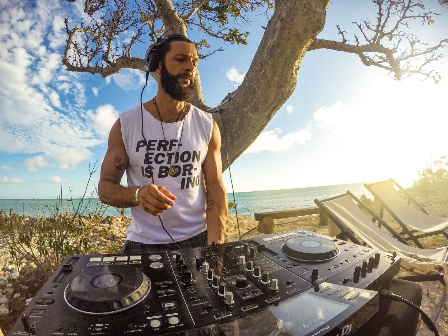 DJ in headphones mixing music outdoors by the beach at sunset