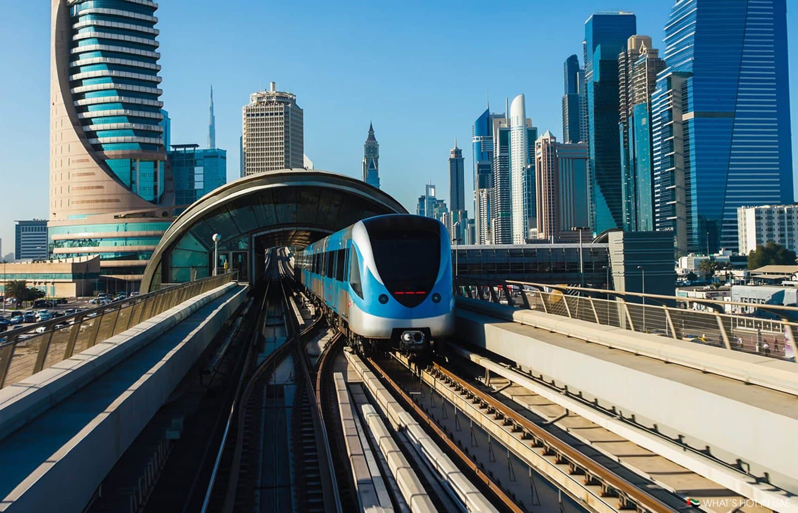 Blue metro train emerging from an elevated station amid a modern skyscraper skyline