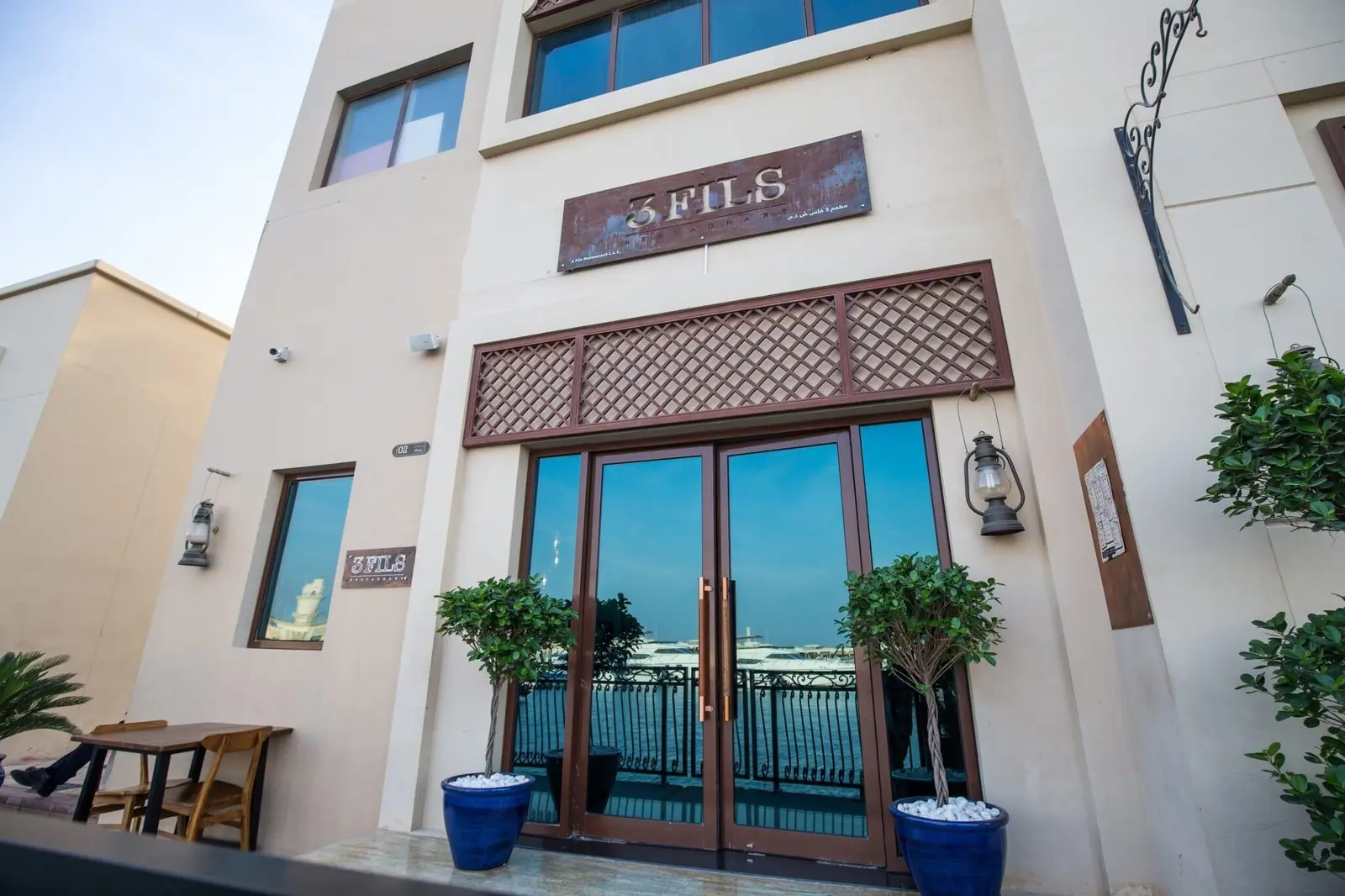 Entrance to 3 Fils restaurant with waterfront view and blue potted plants