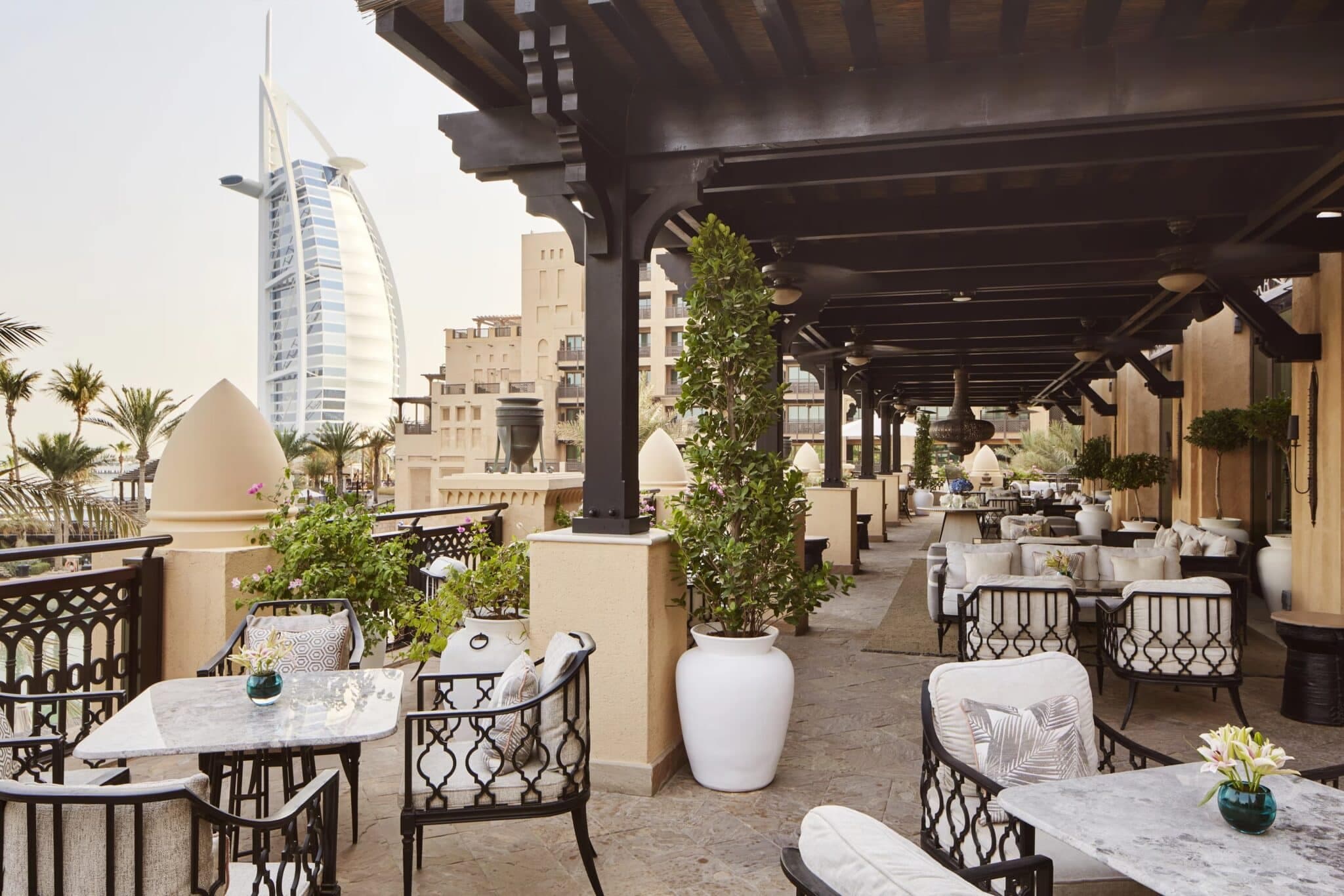 Outdoor terrace lounge with ornate seating, greenery, and views of Dubai’s sail-shaped Burj Al Arab hotel