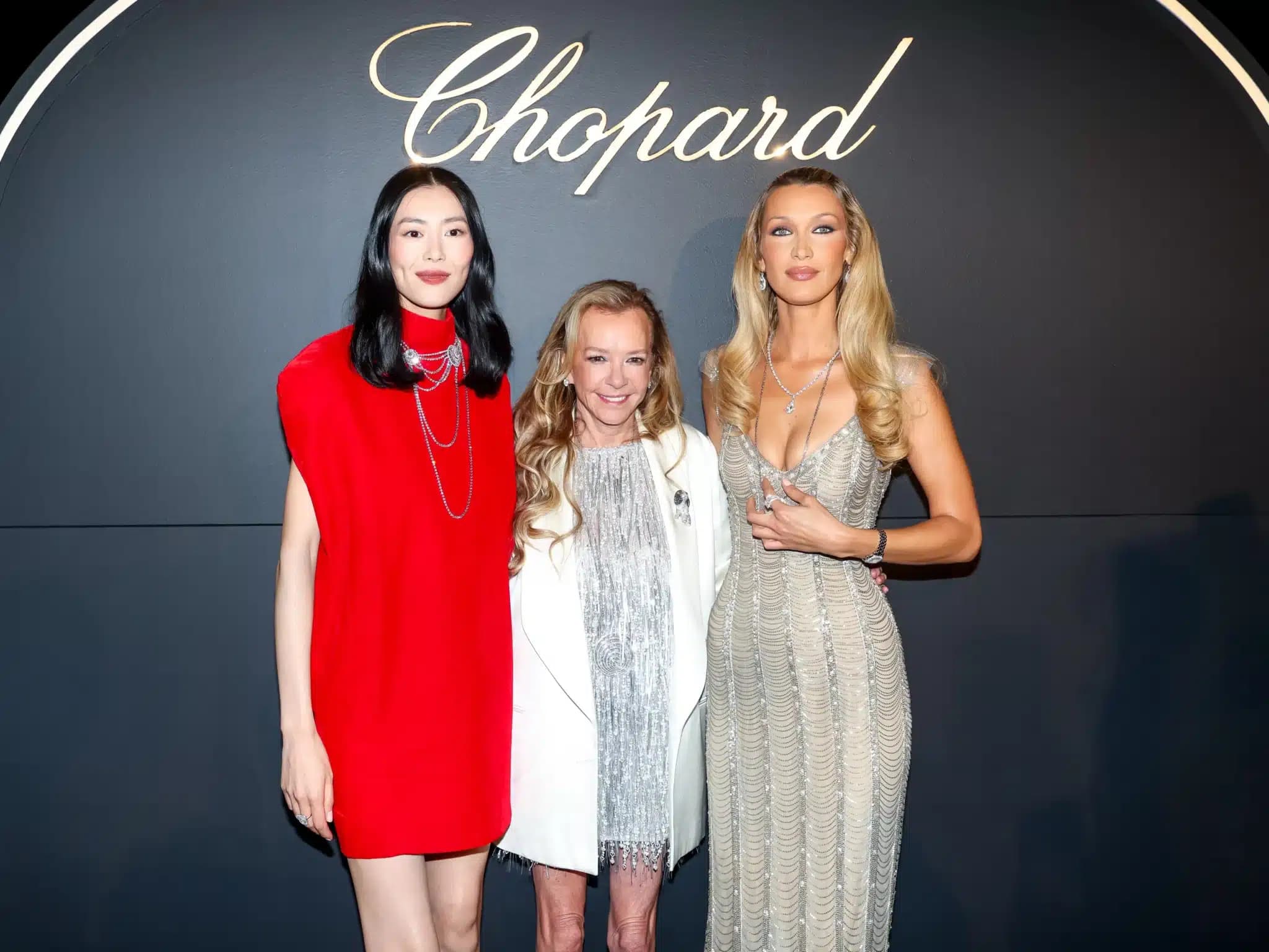 Three women pose in formal attire beneath a “Chopard” sign