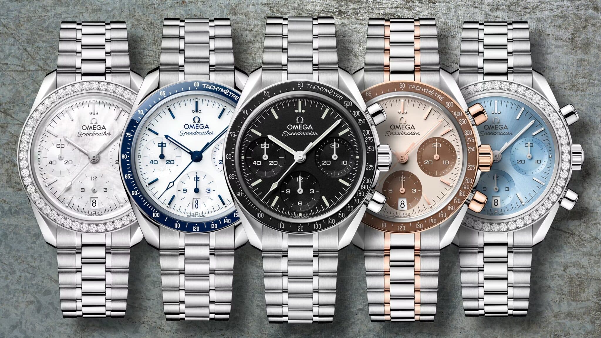 Five Omega Speedmaster watches with white, blue, black, rose-gold, and pale-blue dials arranged side by side