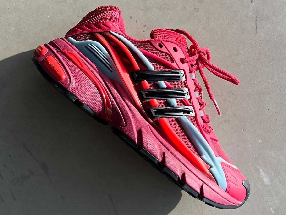Red athletic sneaker with gray and black accents, red laces, and a sculpted sole, shown on a concrete floor