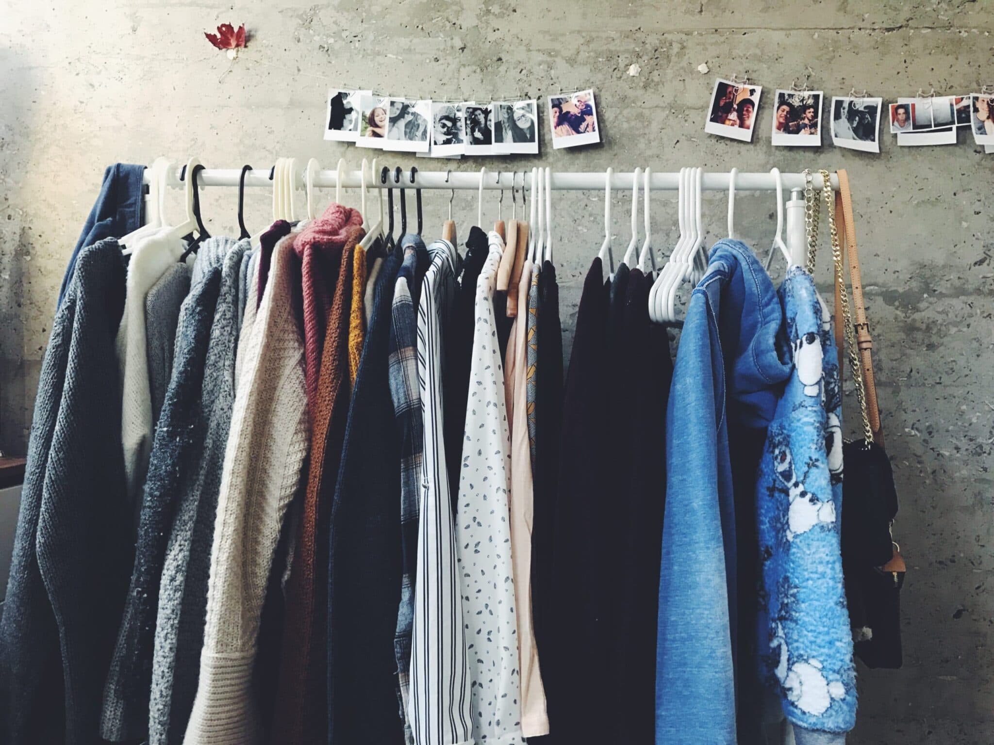 Clothing and scarves hang on a rack beneath a row of clipped photographs