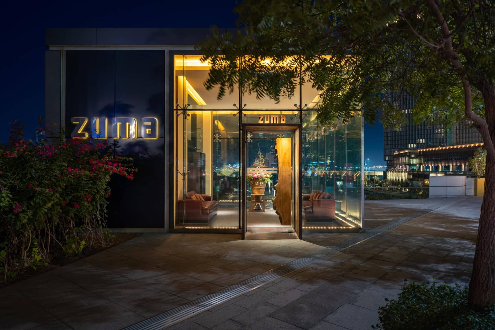 Nighttime exterior of the Zuma restaurant, showing its illuminated glass entrance and “Zuma” signage