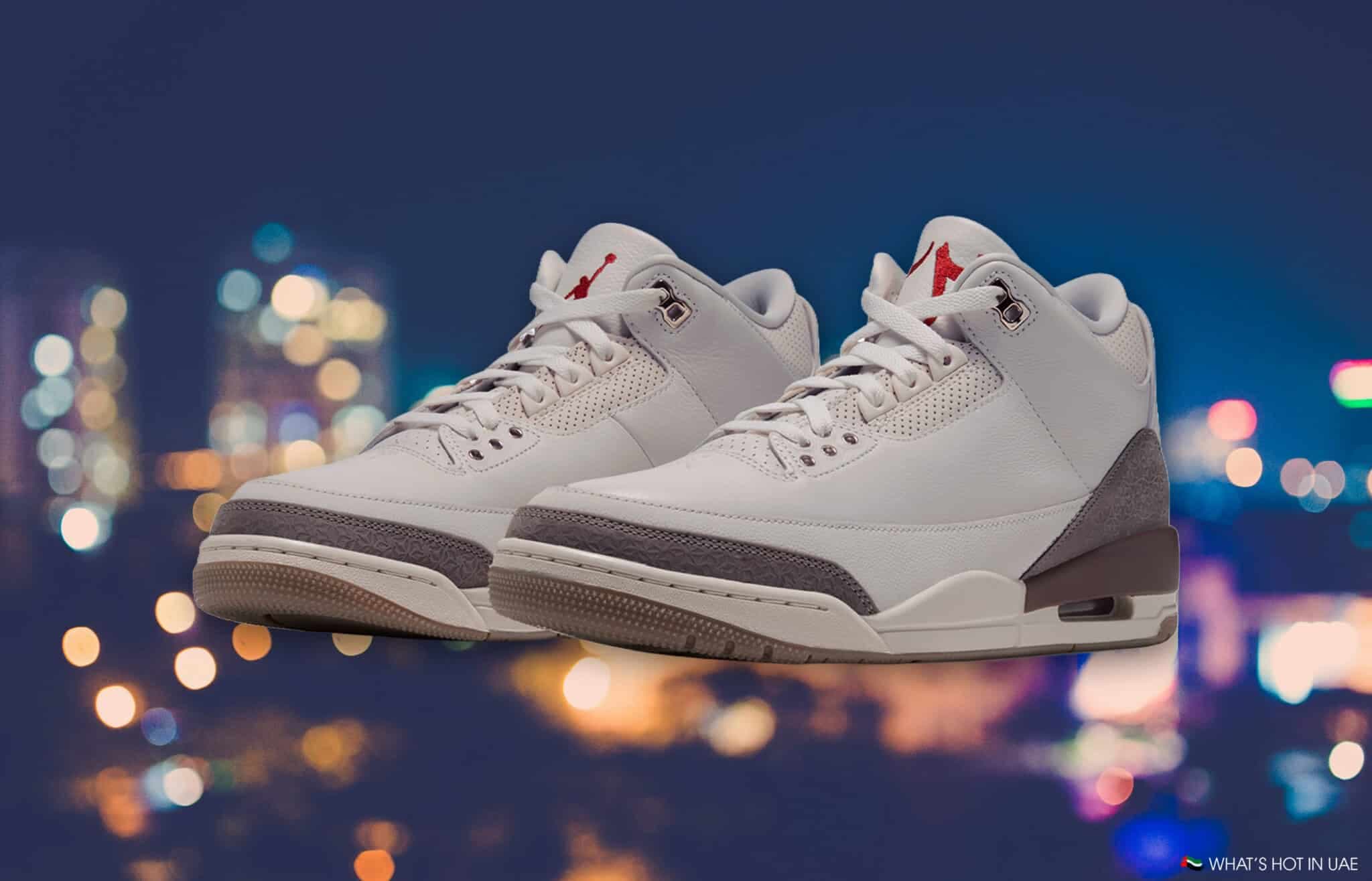 Pair of white high-top sneakers with red accents against a blurred city-light background