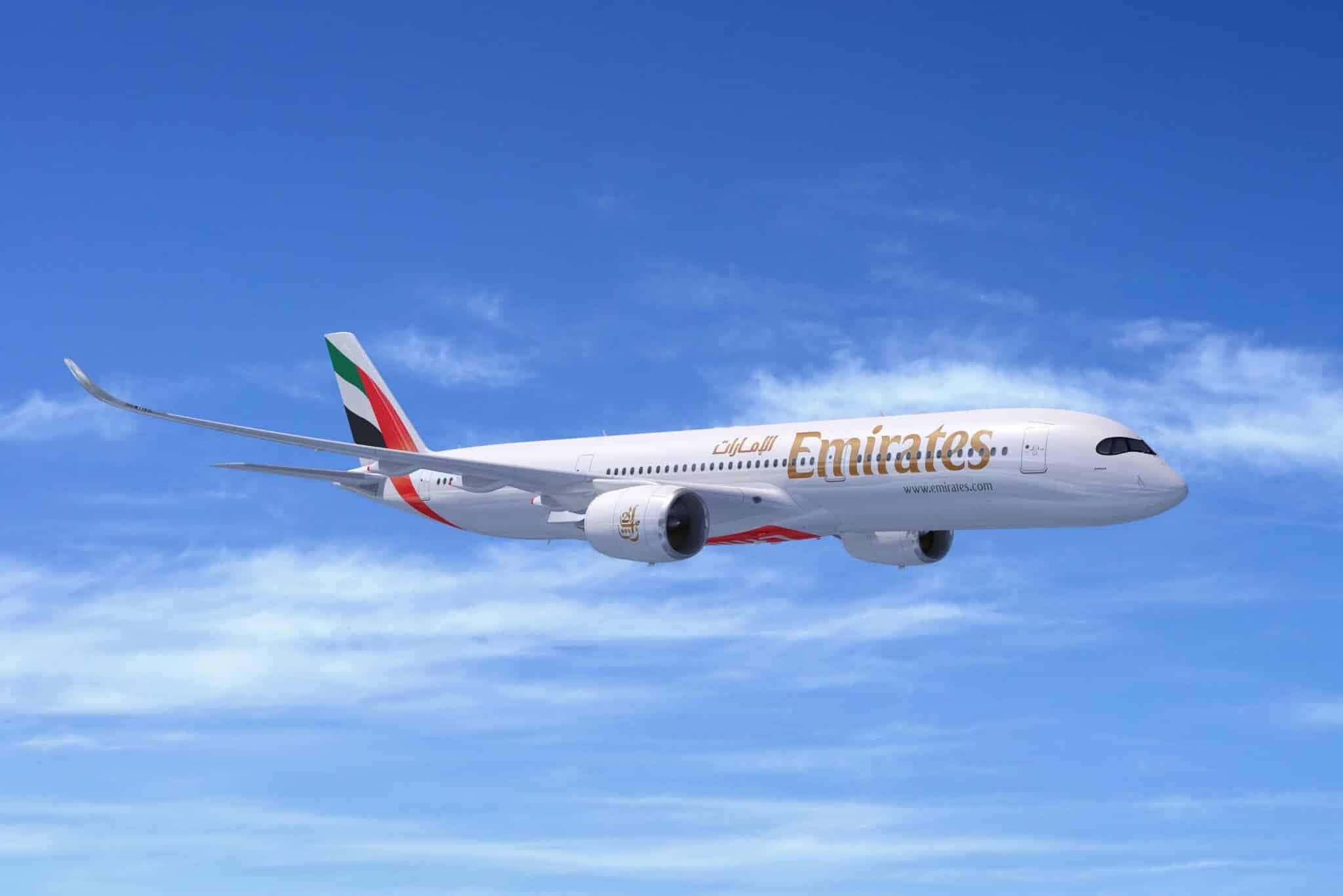 Emirates passenger airplane flying through a blue sky with clouds