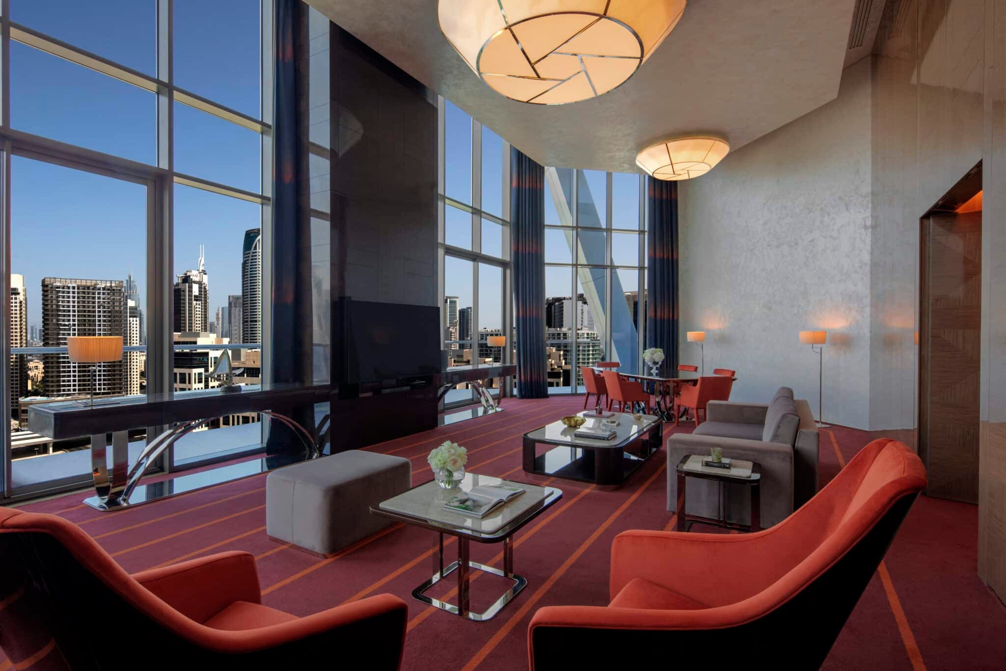 Elegant high-rise lounge with floor-to-ceiling windows, red seating, dining area, and city skyline views