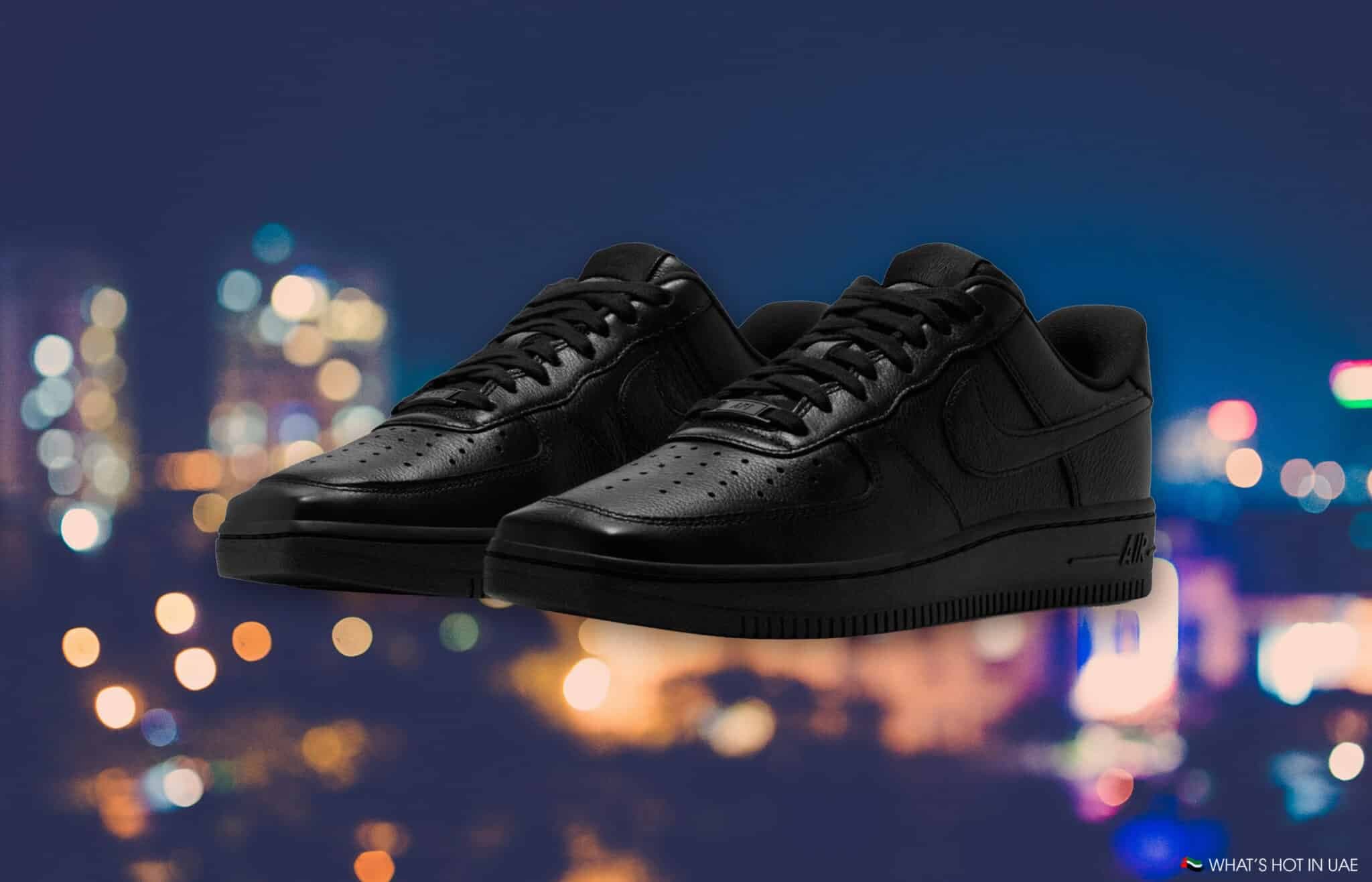 Pair of black low-top sneakers with perforated toes and “AIR” branding, set against blurred city lights