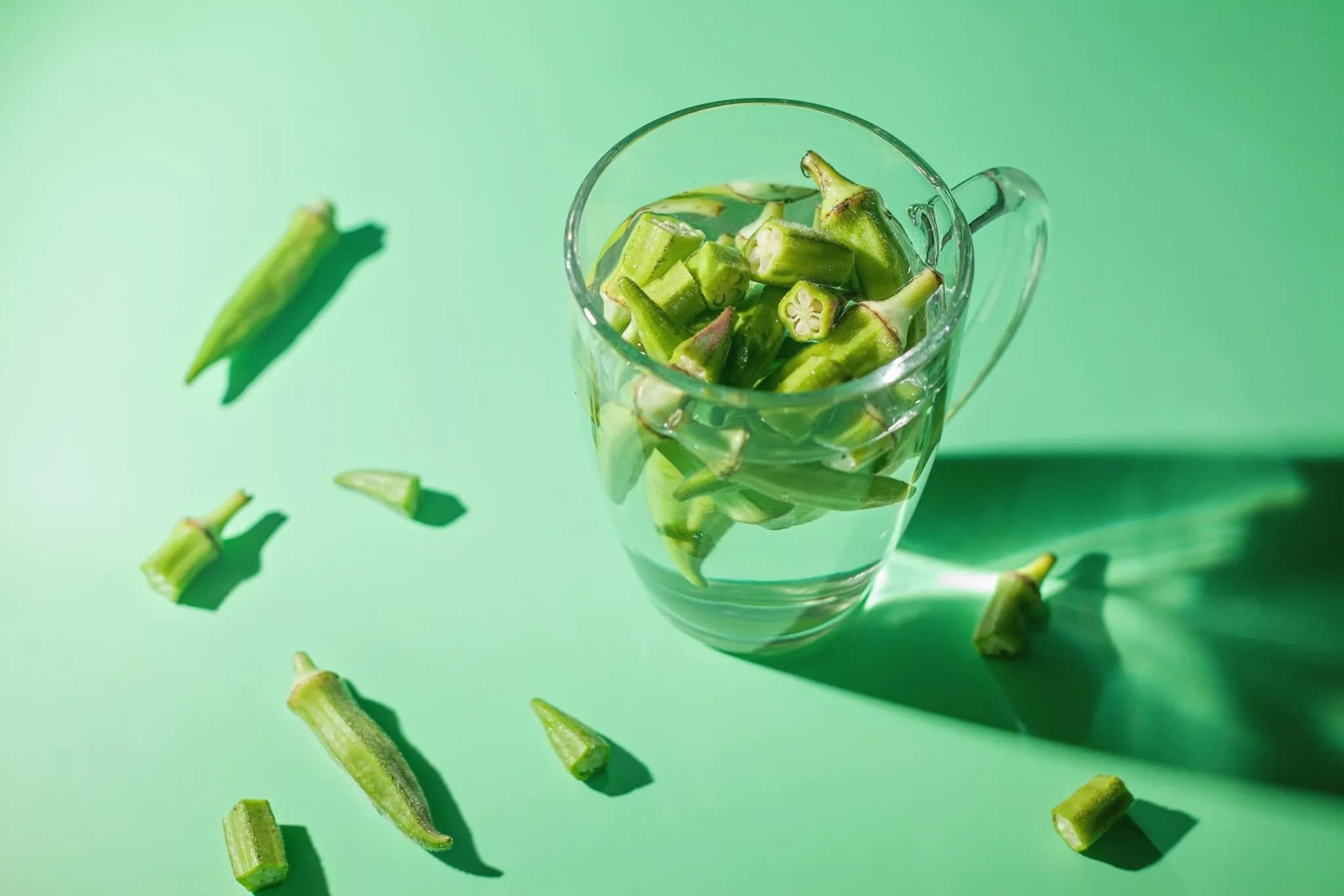 Glass measuring cup filled with chopped okra, surrounded by whole okra pods and cut pieces