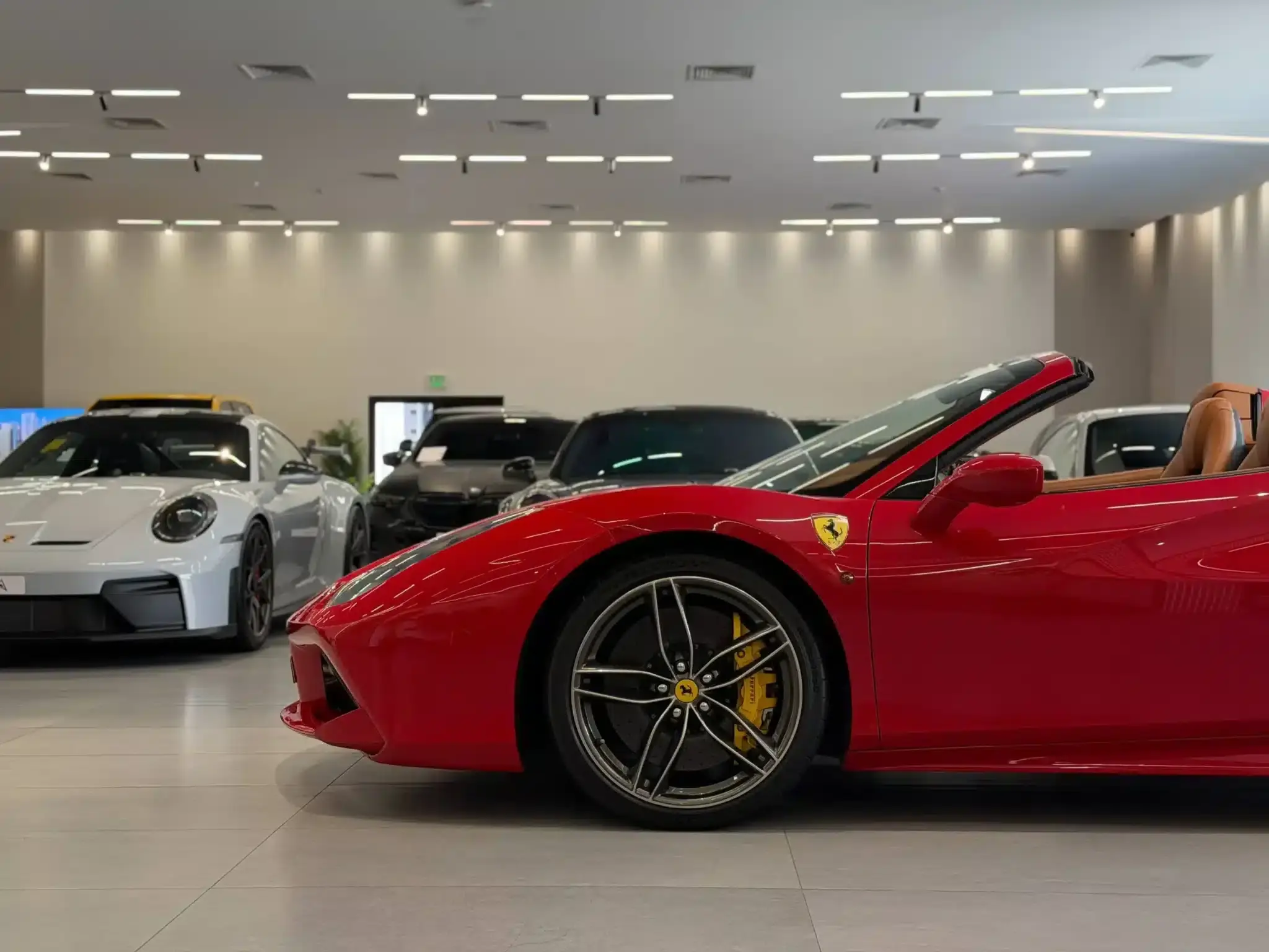 Red Ferrari convertible displayed in a showroom, with several other luxury cars behind it