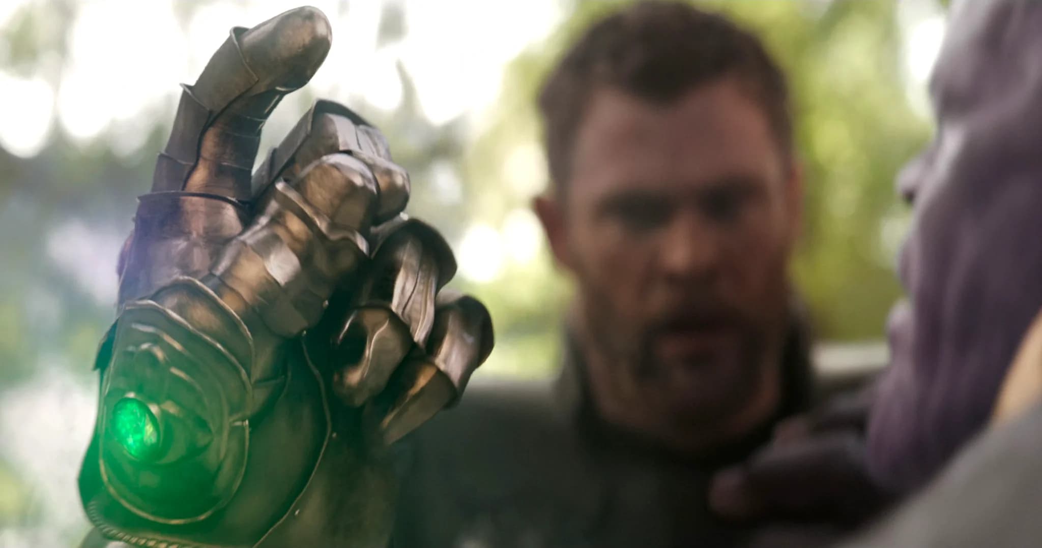 A person in the background looks toward an armored hand holding a glowing green device