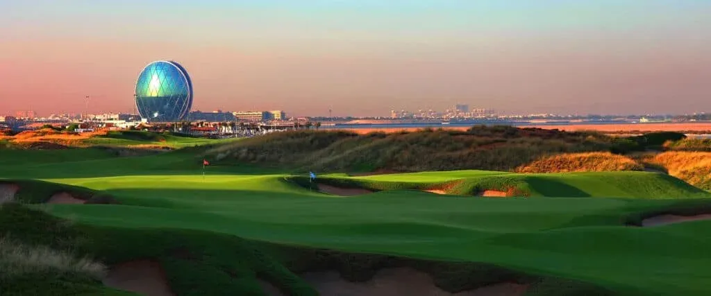 A vibrant golf course landscape featuring a modern, spherical building in the background, with a clear blue sky and sunset hues in the distance.